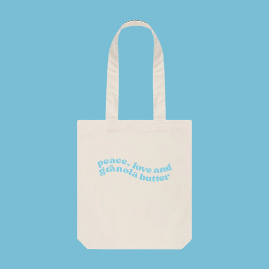 A white tote bag with blue swirly font placed in the centre of the bag, our Granola butter merchandise  