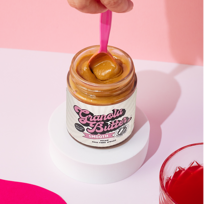 A pink spoon swirling the gluten free and high fibre smooth granola butter in the jar. 
